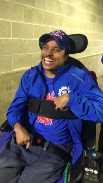 Person in wheelchair smiling, wearing a blue jacket and cap.