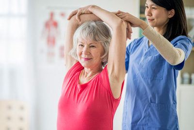 Therapist assisting elderly woman with stretching exercise.