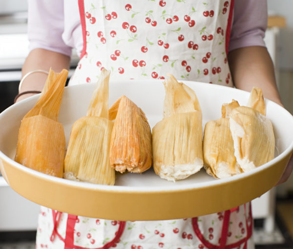 A woman holding a dish of tamales
