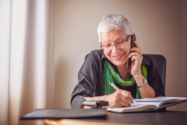 Senior woman drawing a picture in a notebook while taking on cell phone
