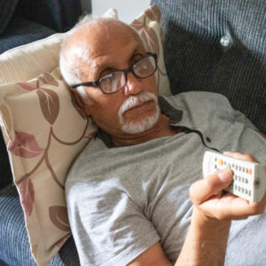 Senior man laying on couch with channel changer