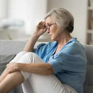 Sad aged woman sit on sofa alone in living room suffers from health issues, life difficulties or fights, retirement bring financial insecurity, causing stress and worries. Regrets, unresolved problems