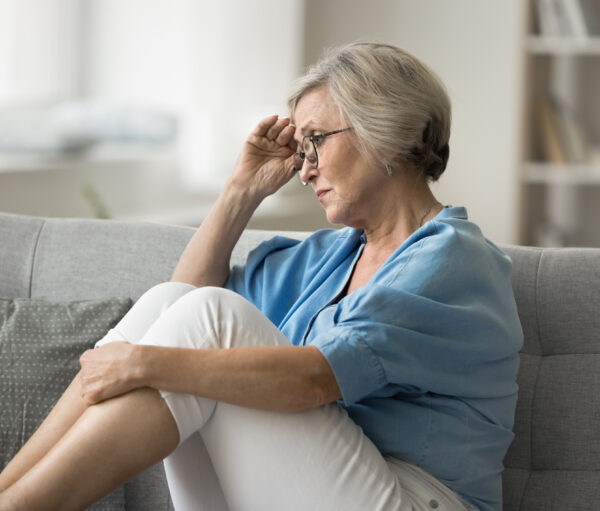 Sad aged woman sit on sofa alone in living room suffers from health issues, life difficulties or fights, retirement bring financial insecurity, causing stress and worries. Regrets, unresolved problems