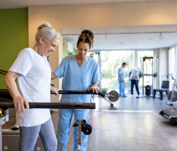 Senior woman in physical therapy walking on the bars with the help of her therapist - orthopedic medicine concepts